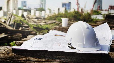 construction hard hat and paper plans in foreground, construction site in background