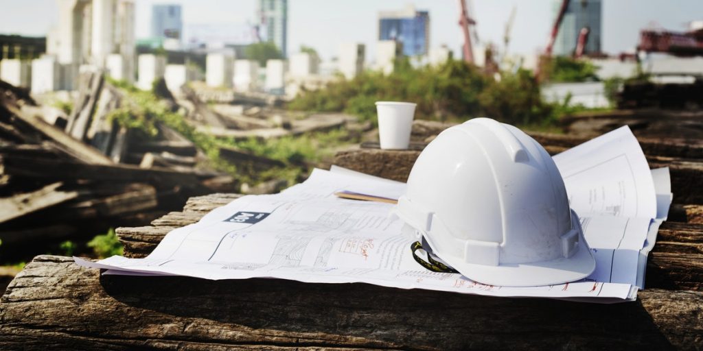 hard hat and paper plans in foreground, construction site in background